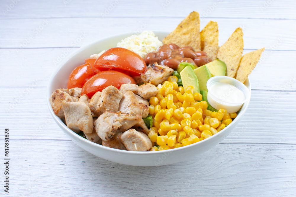 Bowl salad with pieces of roasted pork, grated cheese, beans, corn, tomato, nachos, lettuce, with house mayonnaise