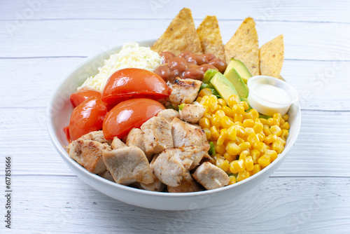 Bowl salad with pieces of roasted pork, grated cheese, beans, corn, tomato, nachos, lettuce, with house mayonnaise