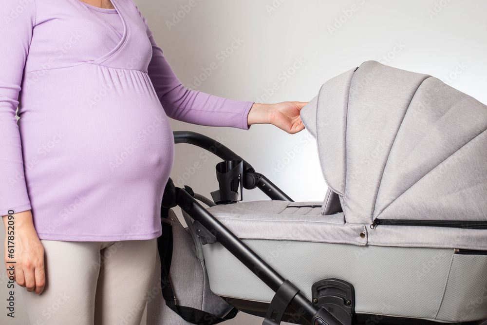 A pregnant girl with a big belly chooses a stroller for her unborn child. Buying a new baby stroller in the store. A pregnant girl with a big belly chooses a stroller for her unborn child. Buying a new baby stroller in the store.