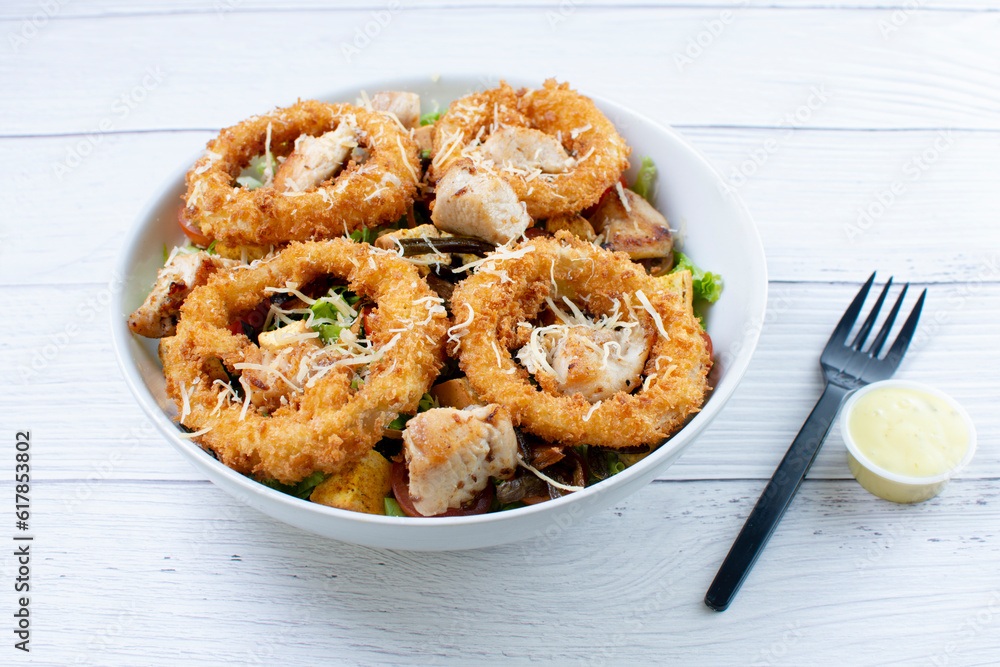 Bowl salad with pieces of roast pork, grated cheese, onion rings and house mayonnaise