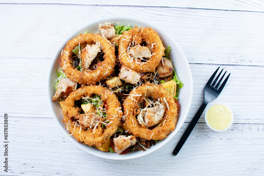 Bowl salad with pieces of roast pork, grated cheese, onion rings and house mayonnaise