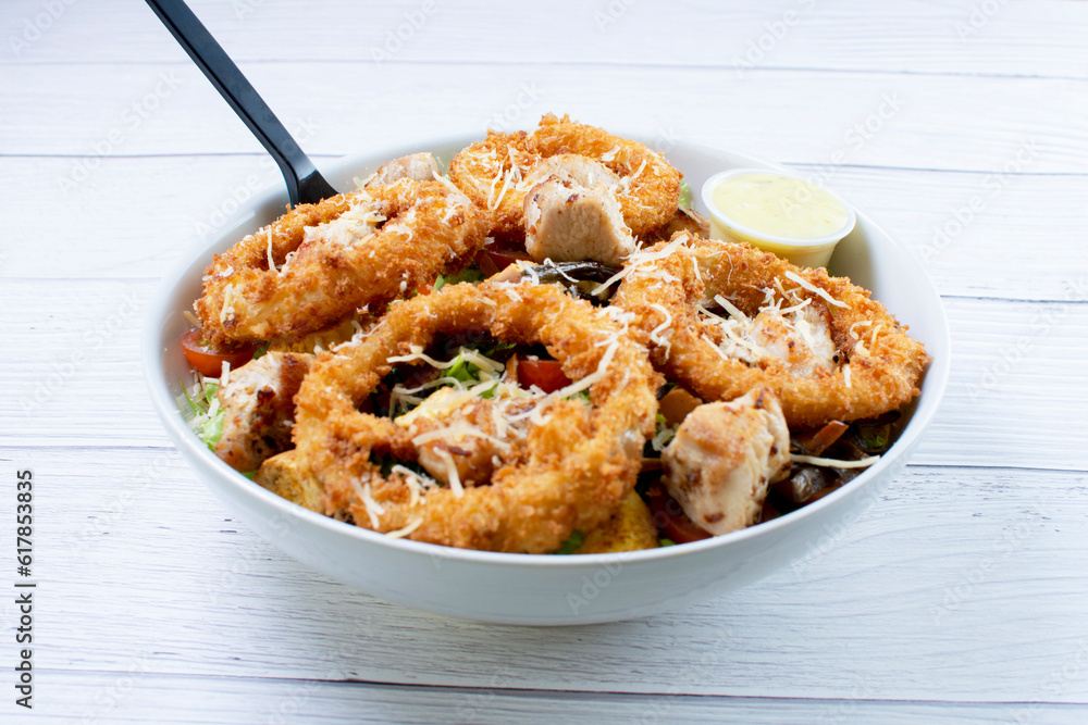 Bowl salad with pieces of roast pork, grated cheese, onion rings and house mayonnaise
