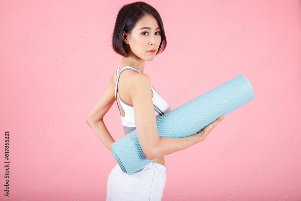 Portrait of woman holding exercise mat roll, holding yoga mat roll on pastel pink background.