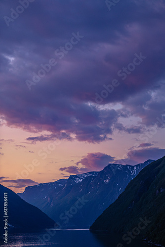 Dramatic colorful twilight summer sunset on the Geiranger fjord in Norway with vibrant clouds steep cliffs and waterfalls