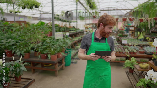 Mobile Male Employee Checking Inventory via Tablet in Flower Shop. Green Aproned Young Man Integrating Modern Tech in Store Operations