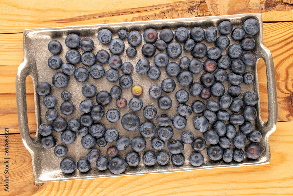 Several ripe blueberries with metal tray on wooden table, macro, top view. Several ripe blueberries with metal tray on wooden table, macro, top view.