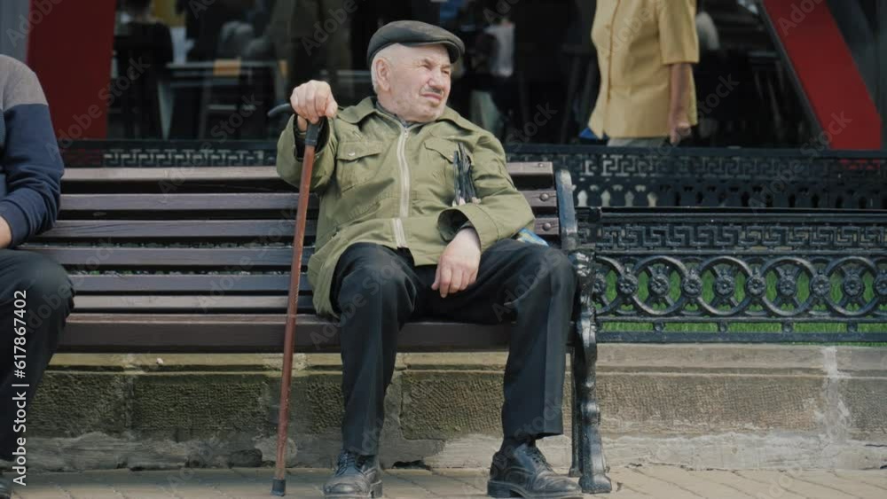 An old man sits on a bench in the park. Portrait of a pensioner on the background of the city An old man sits on a bench in the park. Portrait of a pensioner on the background of the city