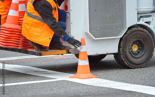 Worker installing traffic cone, pylon on new road marking. Man on road marking machine installing orange safety cone on new marking on the road. Renewal road markings. Road work, renew lane marking