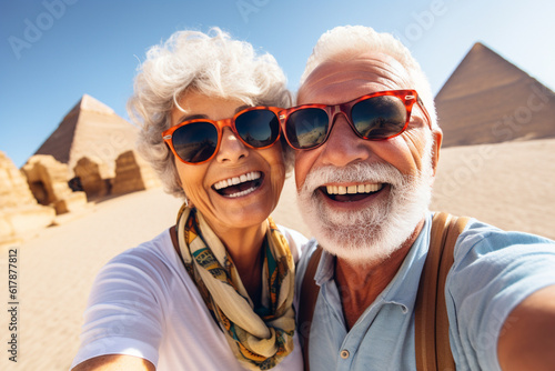 Happy elderly couple tourists take a selfie against the backdrop of the Egyptian pyramids. Travel retirement concept. AI generated.