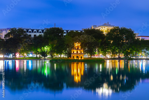 Hanoi City Old Quarters Lake at night glowing with vibrant colourful city lights surrounded by old historic buildings small bridge crossing the lake into a temple on a small island Hanoi Vietnam