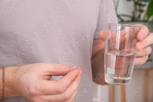 Caucasian man taking a pill and drinking a glass of water. Young man taking vitamin indoors. Health, medicine, treatment concept.