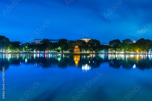 Hanoi City Old Quarters Lake at night glowing with vibrant colourful city lights surrounded by old historic buildings small bridge crossing the lake into a temple on a small island Hanoi Vietnam © Elias Bitar