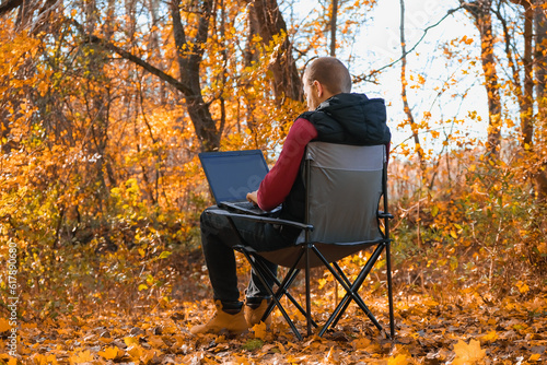 A freelance man works remotely in nature in the autumn forest. Country life. A break from civilization. Van Lifevibes. A man with laptop. Distance learning in the fresh air via a laptop. Remote work.