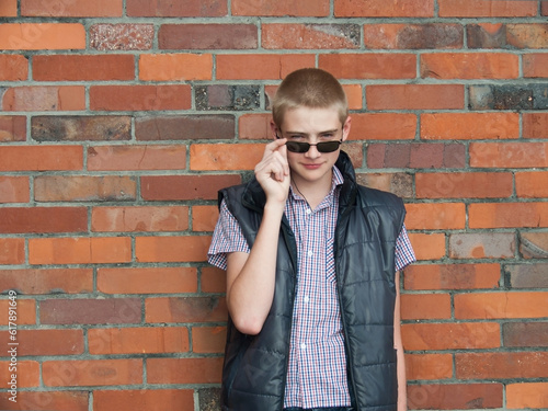 boy stands near a red brick in sunglasses