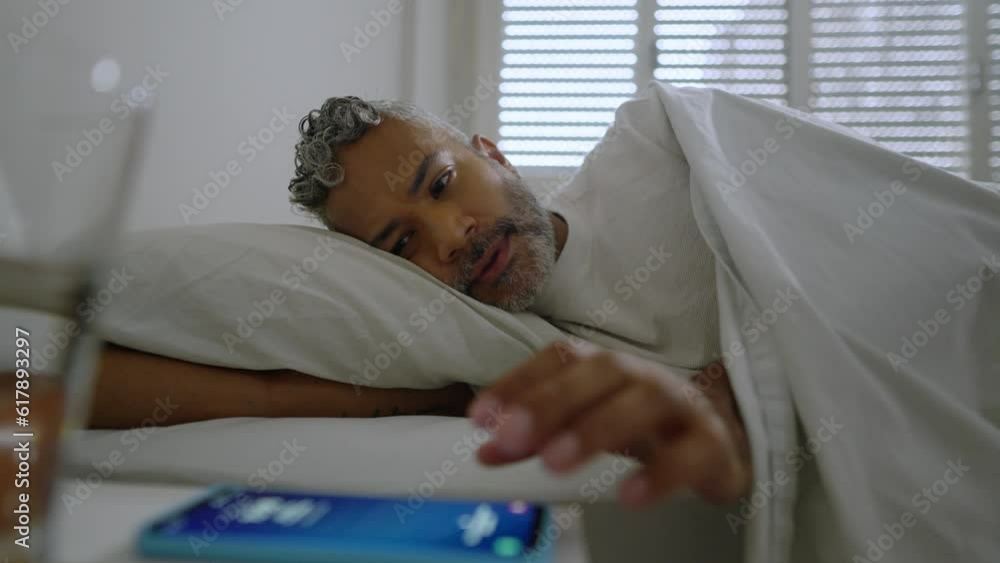 Checking smart phone in the morning. Black man in bed wakes up and look at mobile for messages. Worried and anxious person.