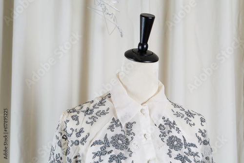 The collar of a button-up lacy blouse on a dress form. Gray floral pattern on a white shirt. 
