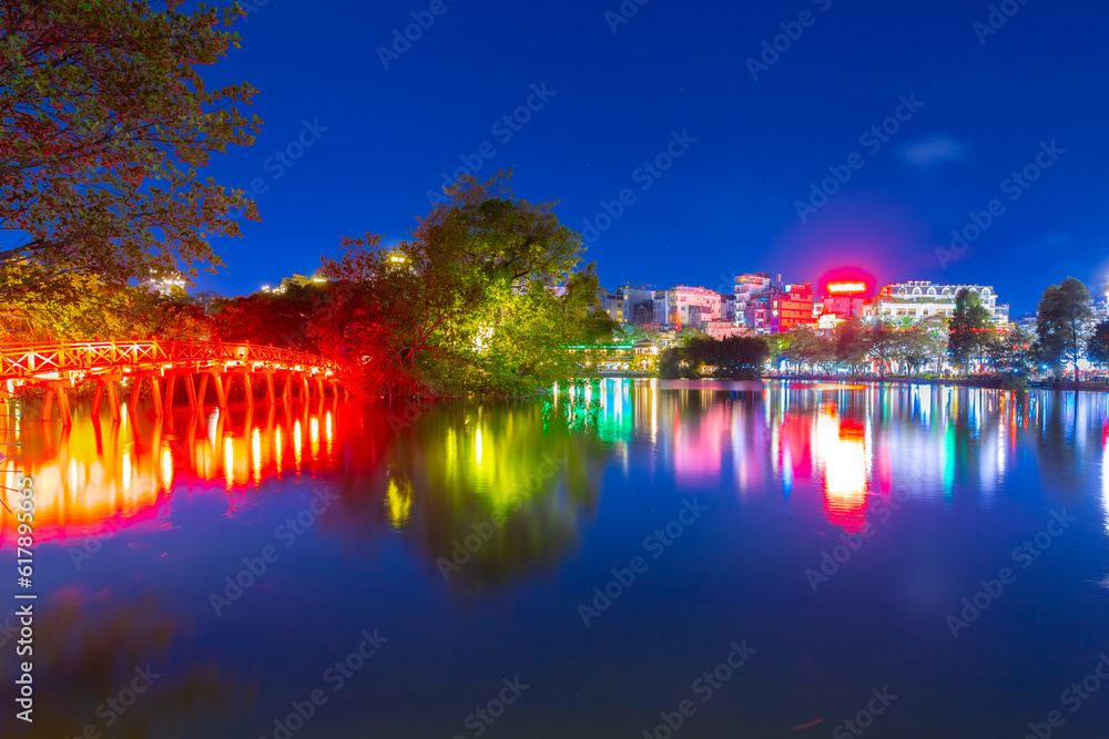 Hanoi City Old Quarters Lake at night glowing with vibrant colourful city lights surrounded by old historic buildings small bridge crossing the lake into a temple on a small island Hanoi Vietnam