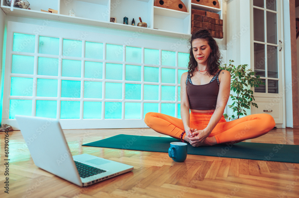 Curly woman sitting in a butterfly pose while hosting an online yoga class. Curly woman sitting in a butterfly pose while hosting an online yoga class.