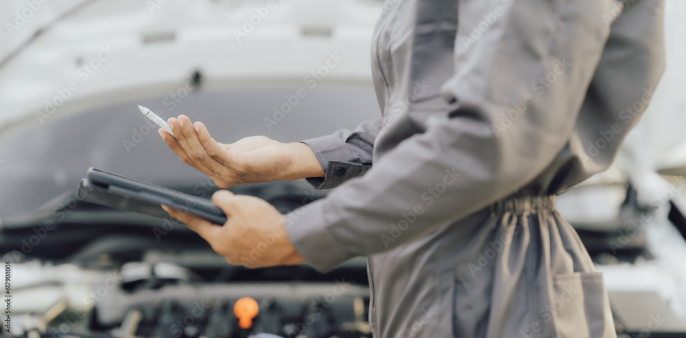 car service, repair, maintenance concept - Asian auto mechanic man or Smith writing to the clipboard at workshop warehouse, technician doing the checklist for repair machine a car in the garage,banner