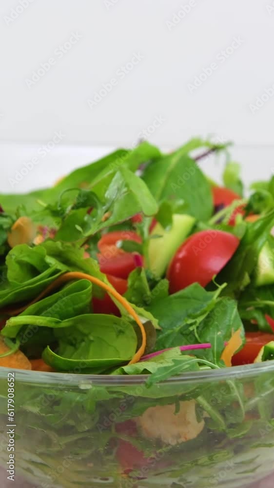 close-up delicious fresh greens salad and tomato glass deep bowl pepper wooden spoons on white background camera slowly shoots around diet food vegetarianism close-up delicious fresh greens salad and tomato glass deep bowl pepper wooden spoons on white background camera slowly shoots around diet food vegetarianism