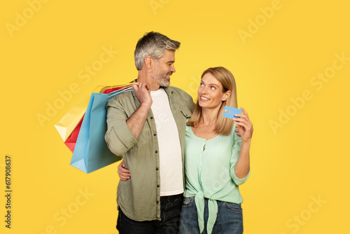 Wallpaper Mural Sales and consumerism concept. Happy middle aged couple showing debit credit card holding shopper bags Torontodigital.ca