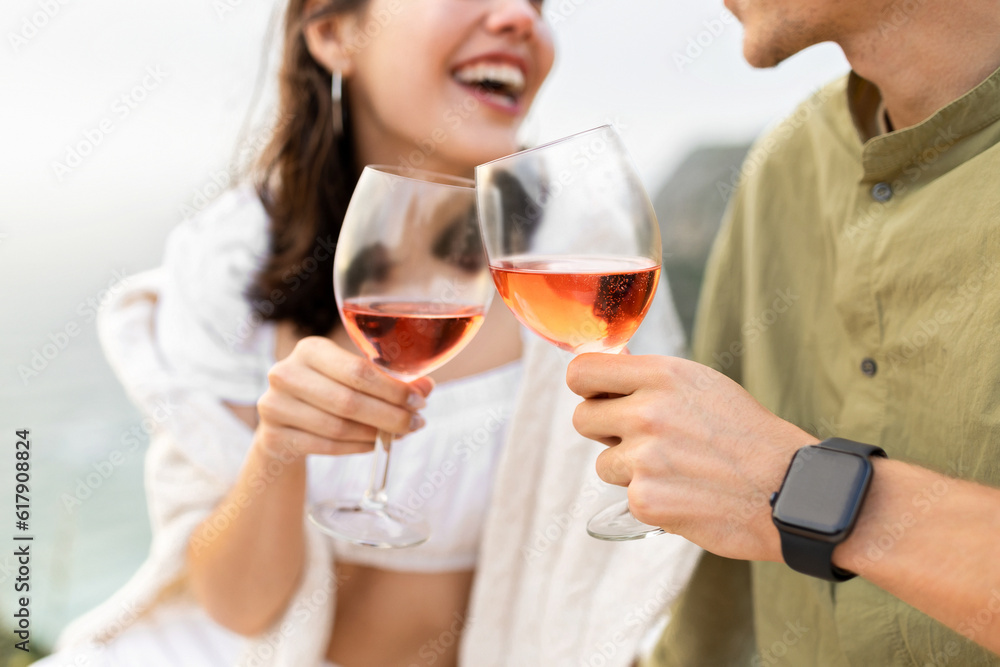 Happy man and woman clanging wine glasses with rose wine, having date and picnic on beach, closeup Happy man and woman clanging wine glasses with rose wine, having date and picnic on beach, closeup