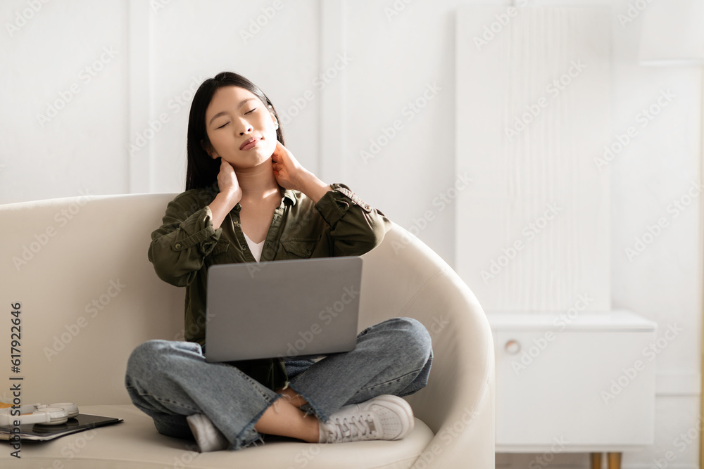 Tired young asian woman independent contractor massaging her neck Tired young asian woman independent contractor massaging her neck