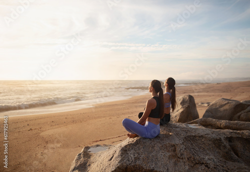 Calm happy young european women twins in sportswear practice yoga on sea beach, enjoy morning peace