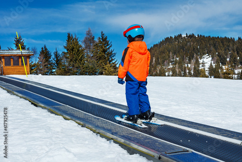 Boy in mask and helmet skiing on moving walkway at ski school