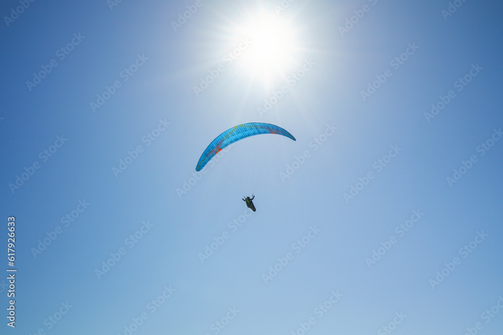 Silhouette of a skydiver with parachute open flying in the air, and bright sun, and blue sky in the background Silhouette of a skydiver with parachute open flying in the air, and bright sun, and blue sky in the background