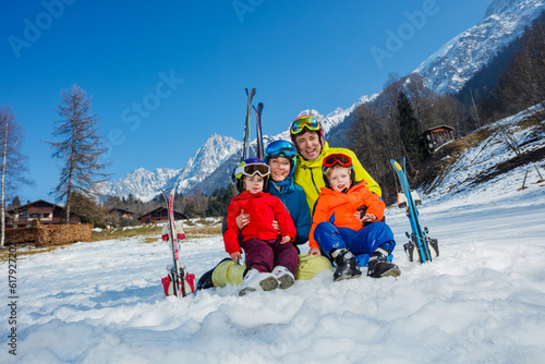 Fun on ski vacation father and kids sit in snow with skis