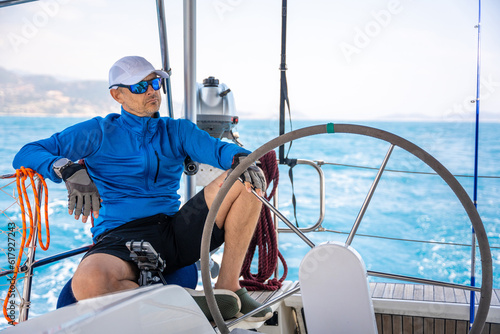 Young man captain stands at the helm and controls a sailboat during a journey by sea