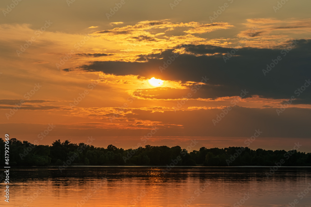 A cloud in the form of an animal eating the Sun at sunset over a river and a forest
