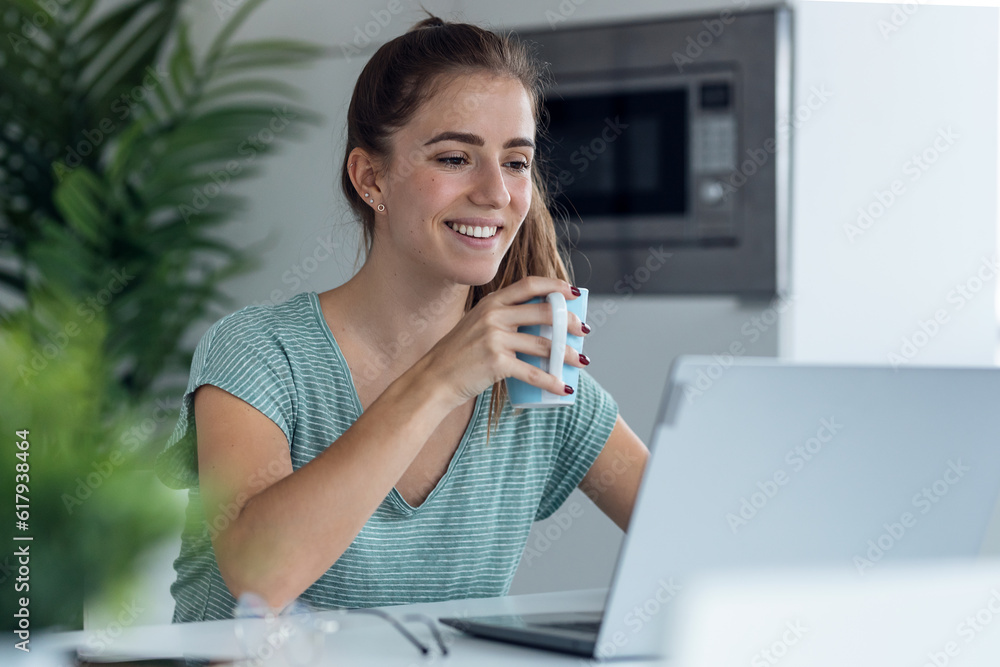 Pretty young woman working with laptop while drinking cup of coffee in the kitchen at home. Pretty young woman working with laptop while drinking cup of coffee in the kitchen at home.