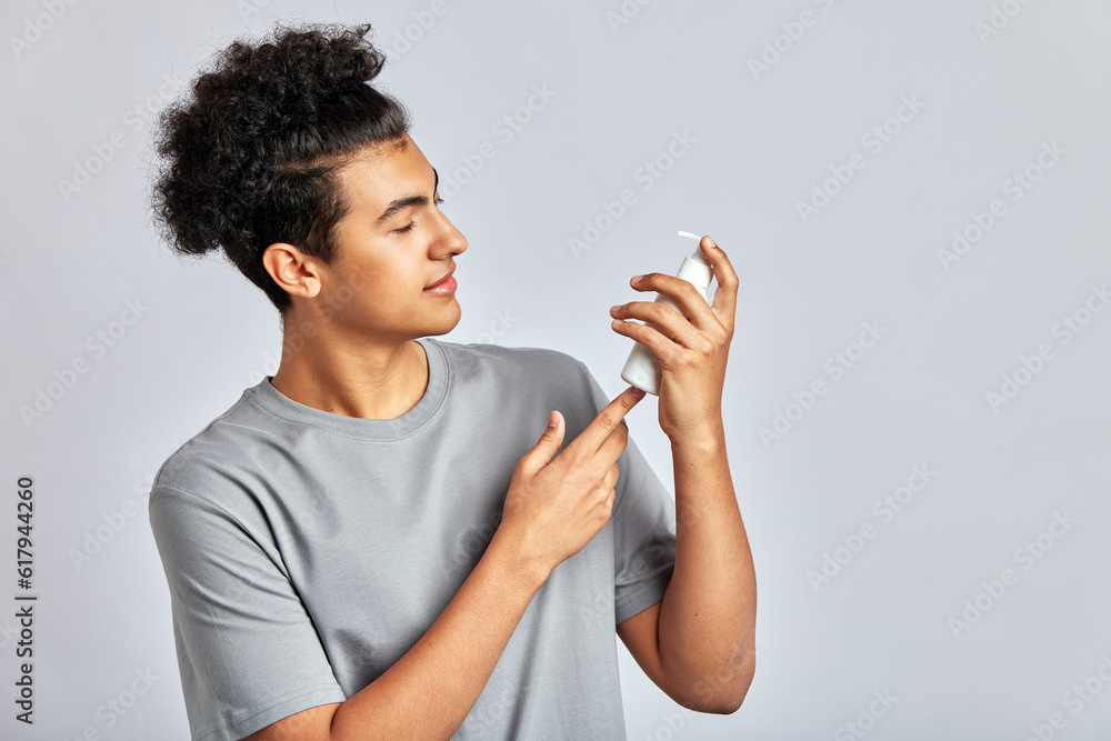 Young handsome smiling guy with black curly hair holding a bottle of facial mask cream in his hands. Man in studio caring for the skin to maintain his youthful and healthy appearance. Men's self-care. Young handsome smiling guy with black curly hair holding a bottle of facial mask cream in his hands. Man in studio caring for the skin to maintain his youthful and healthy appearance. Men's self-care.