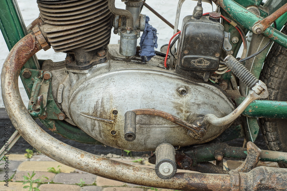 part of a closed old retro rusty  heavy powerful engine in an aluminum crankcase with an exhaust pipe and a winding lever from a vintage motorcycle on the 