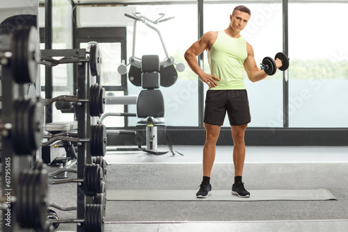 Fit young man in sportswear exercising with a dumbbell at a gym