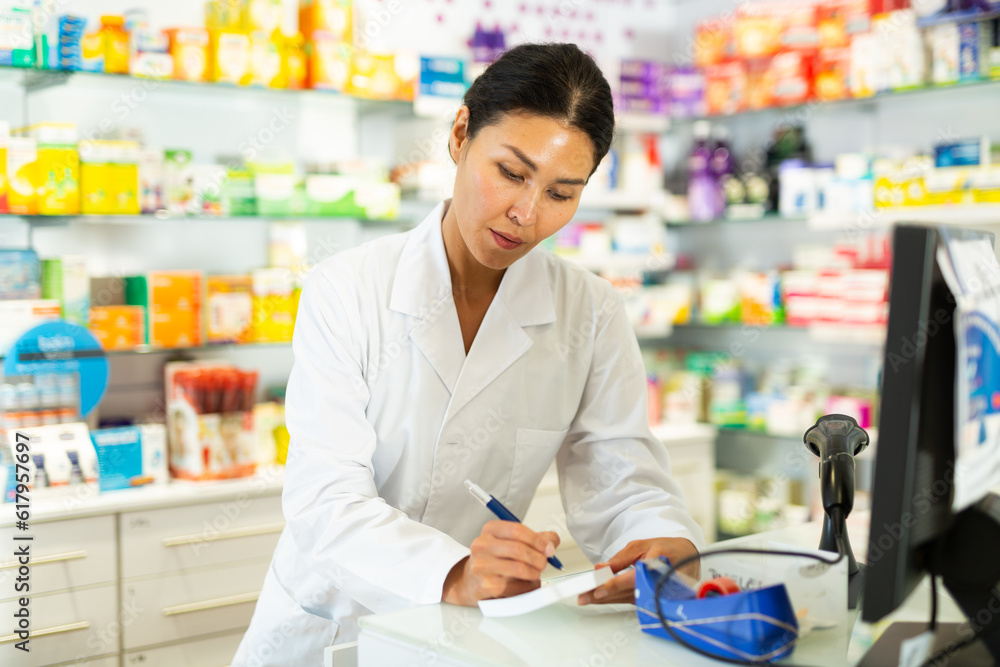 Female doctor or pharmacist working in pharmacy, using computer screen