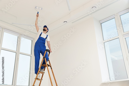 Foto Worker in uniform painting ceiling with roller on stepladder indoors, low angle
