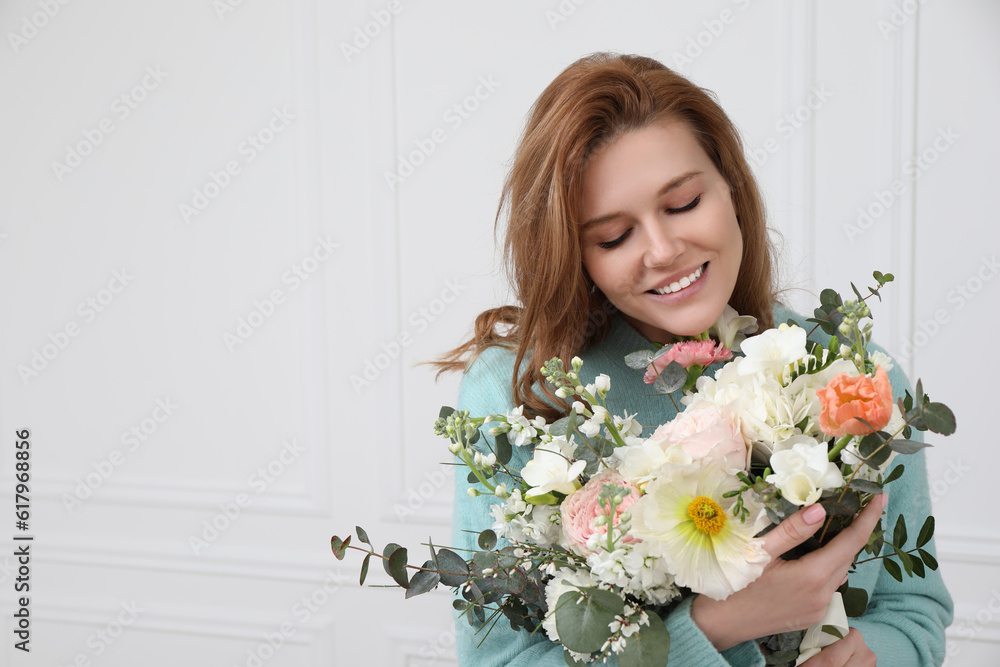 Beautiful woman with bouquet of flowers near white wall indoors. Space for text Beautiful woman with bouquet of flowers near white wall indoors. Space for text