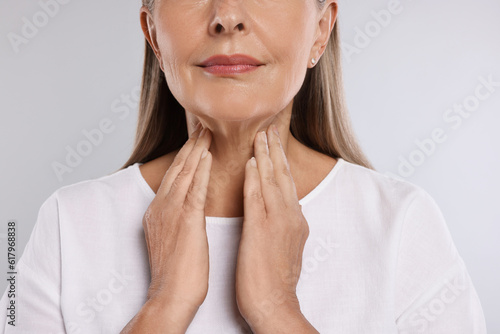 Endocrine system. Senior woman doing thyroid self examination on light grey background, closeup photo