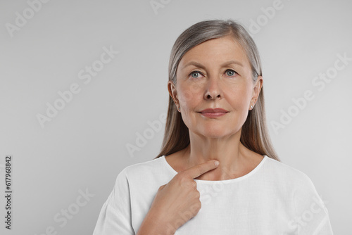Endocrine system. Senior woman doing thyroid self examination on light grey background, space for text