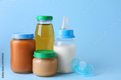 Healthy baby food, juice, milk and pacifier on light blue background