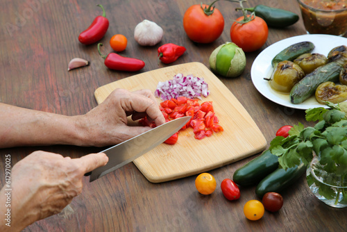 Woman cutting tomato for salsa sauce at wooden table  closeup