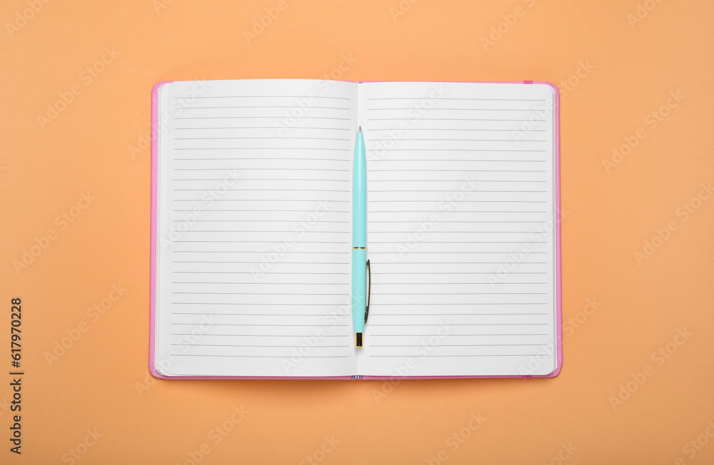 Open office notebook and pen on pale orange background, top view Open office notebook and pen on pale orange background, top view