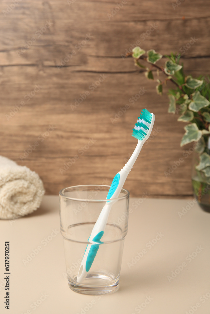 One toothbrush in glass on beige table One toothbrush in glass on beige table