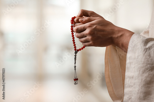 Muslim man with misbaha praying on blurred background, closeup. Space for text