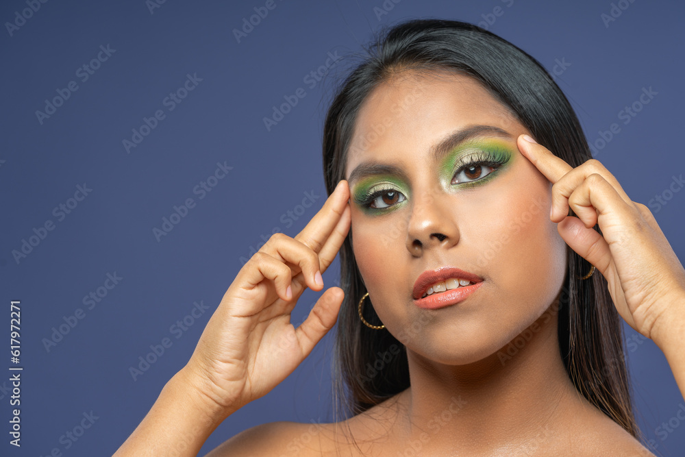 Fototapeta premium Young woman wearing makeup with her hands resting on her face
