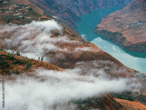 Turquoise colored river bends around mountains surrounded by clouds