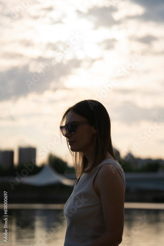 Silhouette of a young woman in sunglasses against the sunset sky.